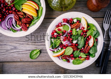 Homemade spinach, apple, pecan, red onion  salad with goat cheese and pomegranate on wooden background