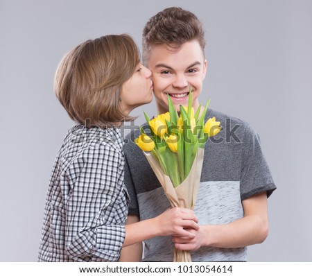 Teen boy and girl in Valentine day, birthday, or holiday. Boy giving tulips for girl. Portrait of happy brother and sister on gray background. Sister kisses brother.