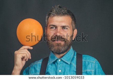 Man with orange balloon. Happy bearded man in blue denim shirt and inflatable balloon in hand. Charming man in good mood. Emotions, feelings and reaction. Copy space for your advertising information.