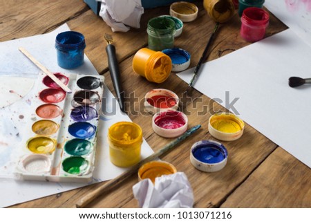 Watercolors Paint, Gouache, Brushes and Paper Sheets on a Wooden Background. The concept of the creative workshop of the artist