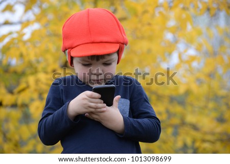 New digital technologies in the hands of a child. Little boy playing with mobile phone in the park in autumn