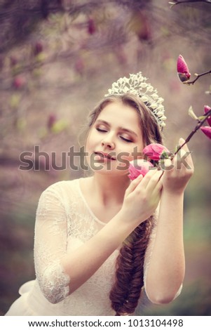 Beautiful young woman with crown in blossom magnolia garden. Spring. 