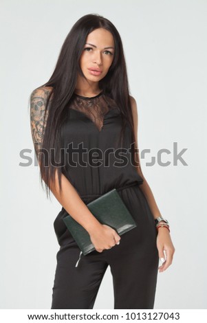 Portrait of a young woman with long dark hair wearing a black dress and holding a planner and a pen. Gray wall background