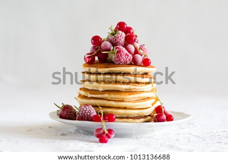 Stack of pancakes with raspberry, red currant, cream and honey on white table cloth Royalty-Free Stock Photo #1013136688