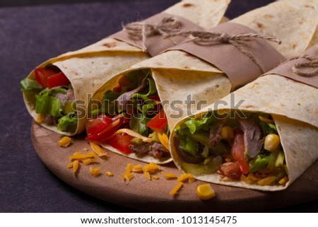 Tortilla, burritos, sandwiches twisted rolls. Wraps with beef, tomatoes, lettuce, cucumbers, cheddar cheese, corn and onion rings. horizontal