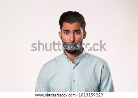Portrait of a young man with tape on mouth over white background