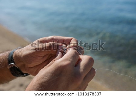 A man knots a fishing hook and lead at the beach Royalty-Free Stock Photo #1013178337
