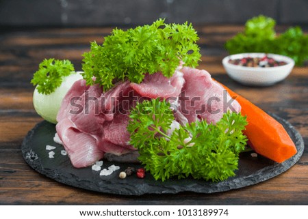 Ingredients for meat broth cooking, raw turkey fillet, carrot, onion, parsley and spices on a cutting board on the wooden table.
