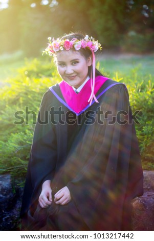 The beautiful Asian woman wearing  black graduate gown and pink chevron portrait in the nature park in the afternoon with flare from the background. 