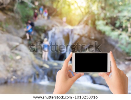 woman use mobile phone and blurred image of the tourists at the waterfall in  Thailand