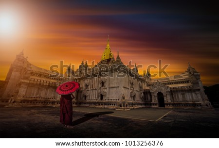 Asian young monk holding red umbrella on the Ananda temple at sunset in Bagan, Myanmar.