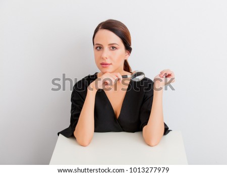 Pretty redhead caucasian woman in black dress with magnifier sitting at white table in lagom style on white background