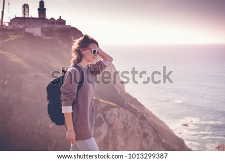 young beautiful woman tourist with a backpack, against the backdrop of Cape Cabo da Roca, portugal, Atlantic coast. Picture with retro toning