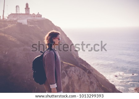 young beautiful woman tourist with a backpack, against the backdrop of Cape Cabo da Roca, portugal, Atlantic coast. Picture with retro toning