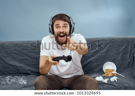  garbage on the couch, joyful man with headphones playing the console with a joystick on a blue background                              