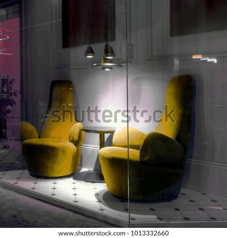 Soft armchairs, small round table and near chandelier lamp with light against grey wall behind clean glass