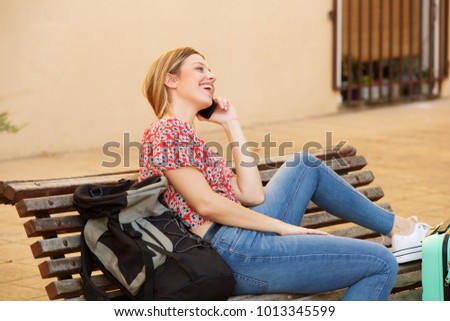 Portrait of female traveler sitting with bags and talking on mobile phone