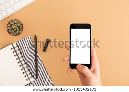 Man student hold an smart phone over beige desk with supplies and succulent cactus.