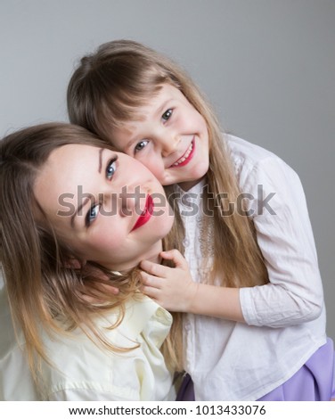 Beautiful little girl and woman, has happy fun smiling face, long blonde hair, pretty eyes, white shirt. Family portrait. Creative concept. Close up. Mom and daughter, relationship love