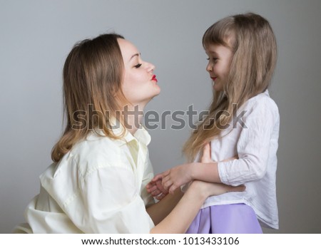 Beautiful little girl and woman, has happy face, long blonde hair, pretty eyes, white shirt. Family portrait. Creative concept. Close up. Mom and daughter, relationship love, kiss and embrace.