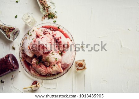 Chicken raw meat shin, drumsticks on wooden cutting board round, spices for cooking chicken drumsticks rosemary, dill, parsley, lemon, salt on gray background