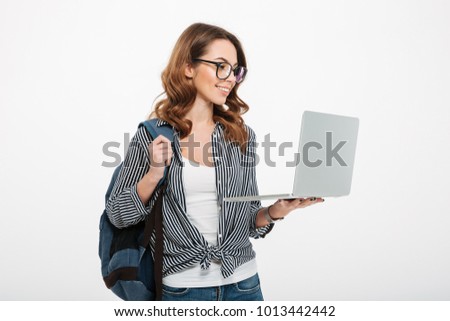 Photo of pretty young lady student standing isolated over white wall background using laptop computer. Looking aside.