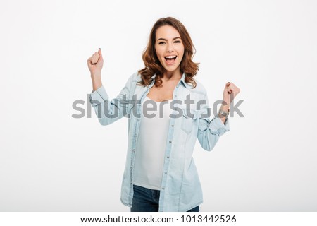Photo of cheerful beautiful young woman standing isolated over white wall background. Looking camera showing winner gesture.