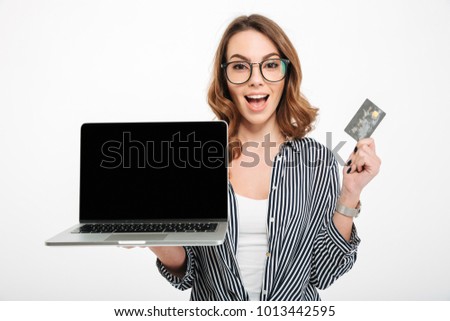 Photo of cheerful young lady standing isolated over white wall background showing display of laptop computer. Looking camera holding credit card.