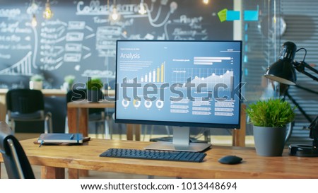 Personal Computer with Mobile Application Design Showing on the Monitor Stands on the Office Desk, In the Background Man Working in the Daytime Office Environment.