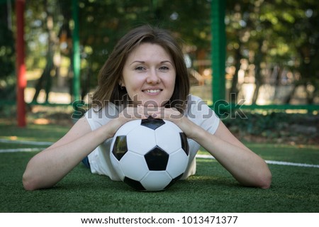 Portrait of a young woman posing at a sports field, having put her head on the soccer ball