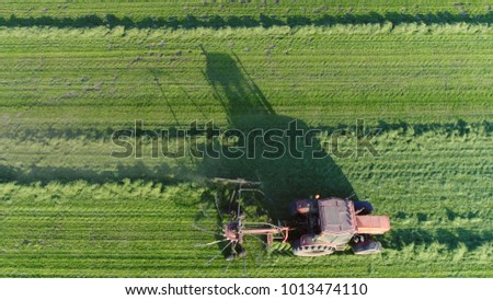 Aerial picture top down photo red tractor raking dries grass and lining it up for future pickup the dried grass will be used as animal fodder for winter feeding of cows and other domesticated animals