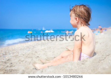 Little child on sandy beach of sea looking at waves. Child on the sea on clear sunny day. Relax on the beach with children. Kid on white sand on the beach