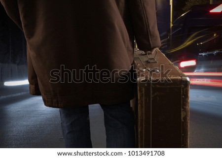 man from behind holding case and walking on the street at night