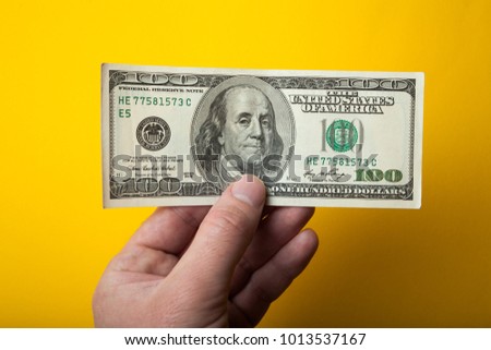 A hundred dollars in hand on a yellow background.