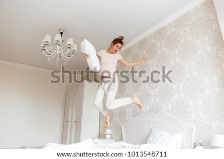 Full length image of Playful young woman having fun on bed with cushion at home