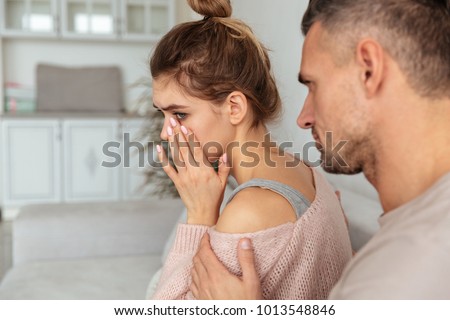 Back view of Careful man sitting on couch and calm down his upset girlfriend which crying at home