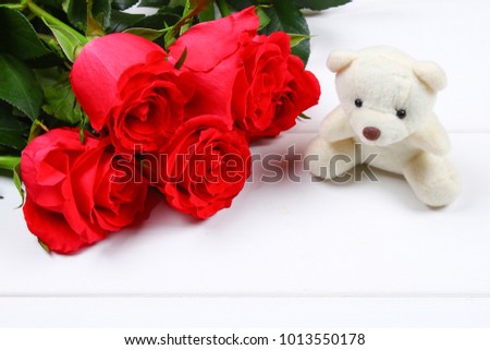 White teddy bear surrounded by pink roses on a white wooden table. Template for March 8, Mother's Day, Valentine's Day
