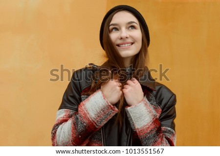 Young girl in winter clothes on orange background. Uplifted mood, naive and dreamy look in the sky. Royalty-Free Stock Photo #1013551567