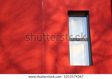 Close up view of a rectangular vertical window in a red wall. Isolated element on a painted surface. Detail of a colorful facade building and one window. Abstract urban picture. Minimalist figure.
