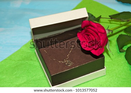 White box with jewelry and next to a red rose. Light green Background. Gift for Valentine's Day or women's day.