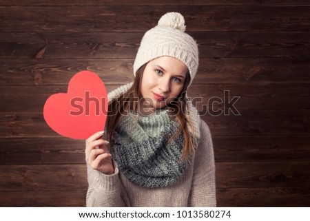 
Beautiful happy girl with Valentine Gift heart. Smiling surprised model girl in winter cloths. Wooden background.