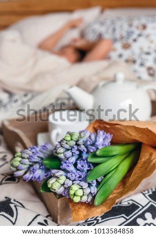 Bouquet hyacinth flowers and teapot with fresh tea are on bed for sleeping person
