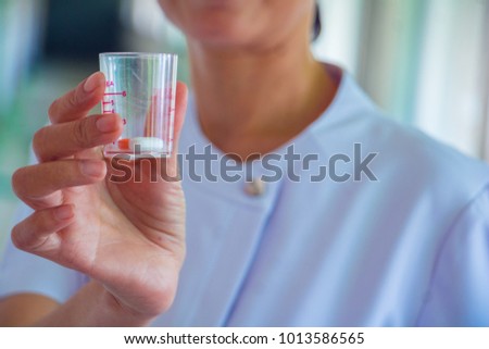 A nurse holding medicine  cup. She is right hand holding it. She is smile and good mood. The photo shows the principle of caring and good health.