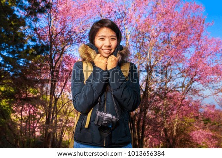 Beautiful Asian woman carry bag and camera in the park with pink cherry blossom flowers, travel theme portrait.