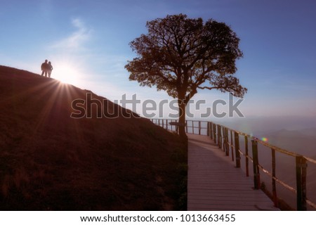 Couple silhouette on hill and lonely tree, The sun is falling down behind with lights flare. On the top of Doi Pui Co,  Popular tourist attraction in Mae Hong Son, Thailand.