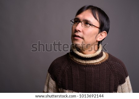 Studio shot of young Asian nerd man wearing turtleneck sweater against gray background