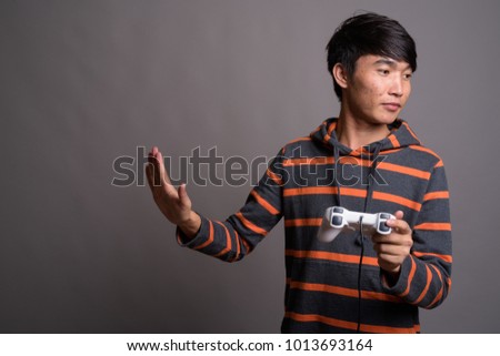Studio shot of young Asian man playing games against gray background