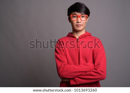 Studio shot of young Asian man wearing red jacket with matching red eyeglasses against gray background