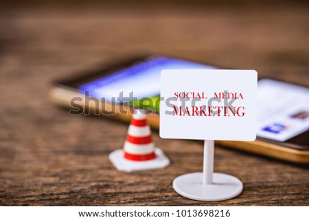 tiny sign with social media marketing text and traffic cone over blurred smart phone or cellphone on wooden floor, image for social media marketing online concept