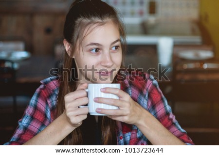 Beautiful young girl drinking tea in restaurant while waiting friend.
Cheerful attractive young woman having delicious coffee in the cafe.